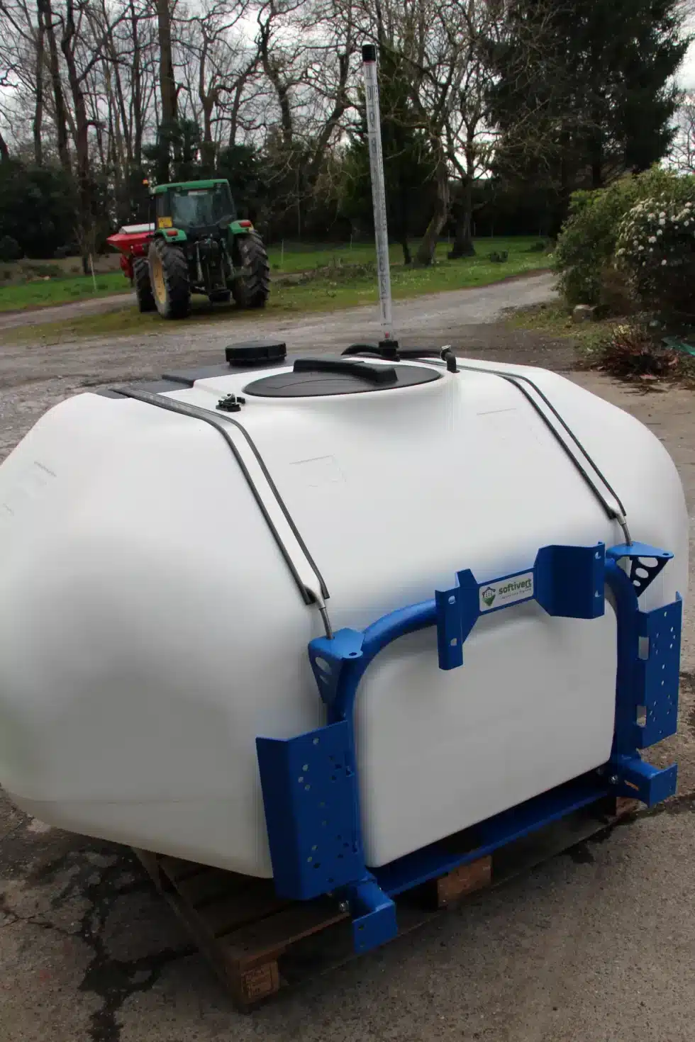 Réservoir blanc sur palette, tracteur en arrière-plan.